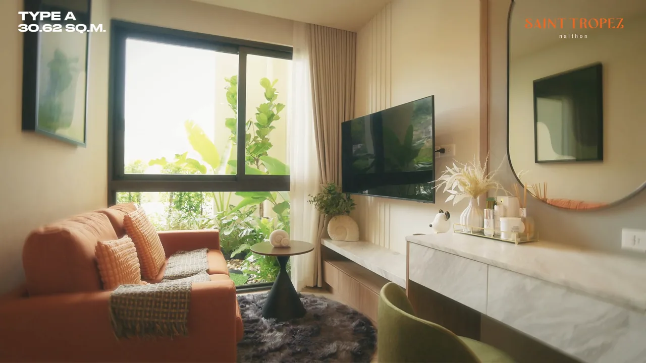 Musterwohnung Studio A mit 30,62 m² im Saint Tropez Naithon: Sofa am Fenster, Fernseher und Schminktisch – Standbild aus dem Videorundgang